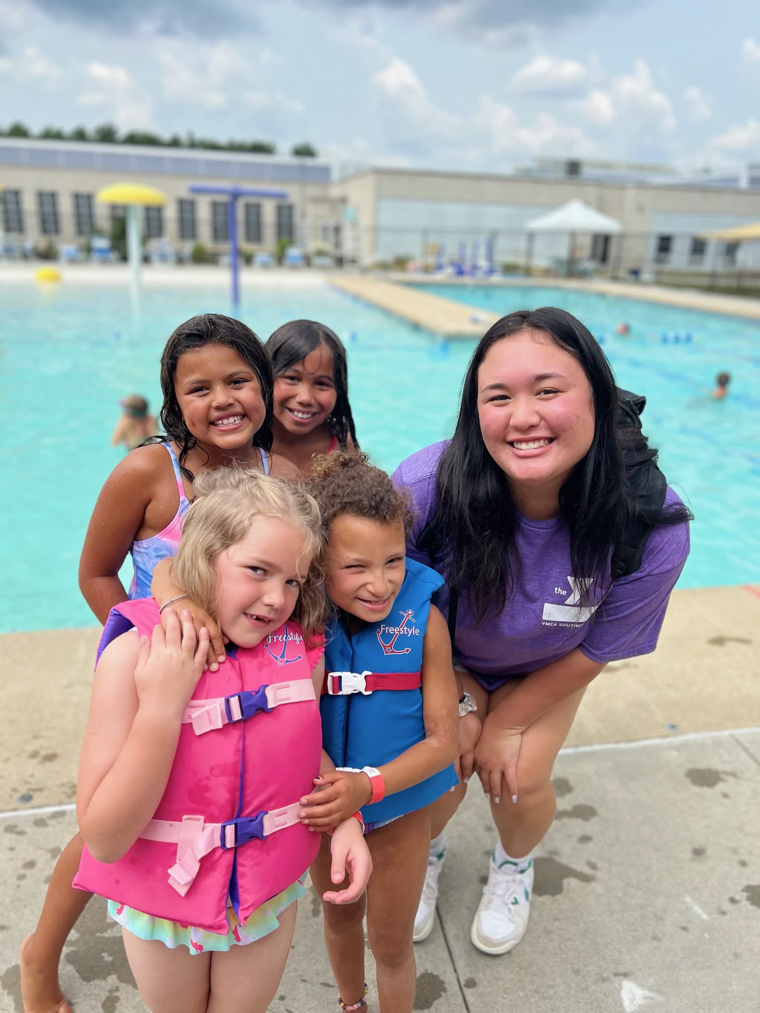 Children near a YMCA pool with an instructor, they are all smiling and having fun